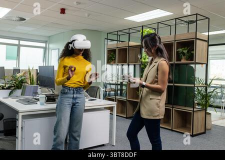Diverse coworkers testing VR headset and using smartphone in open-plan office, copy space Stock Photo