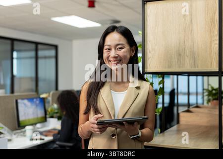 Diverse coworkers wearing business attire holding tablet and typing on computer in open-plan office Stock Photo