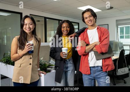 Diverse coworkers holding coffee cups and carrying tablet while standing in bright open-plan office Stock Photo