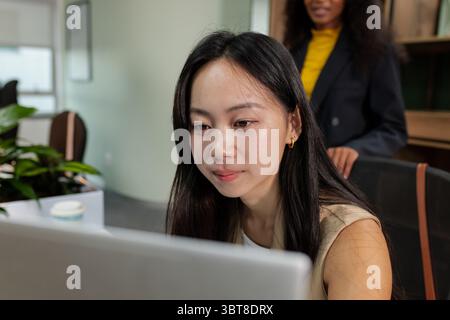 Diverse coworkers collaborating on laptop at office desk with potted plant and coffee cup Stock Photo