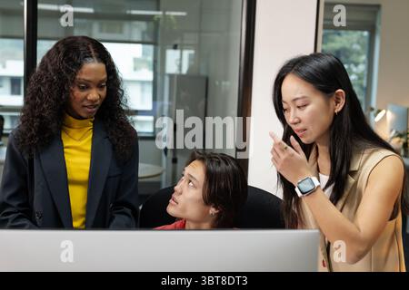 Diverse coworkers in business attire brainstorming ideas around computer monitor at desk in office Stock Photo