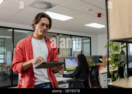 Diverse coworkers collaborating on project in open-plan office using tablet and desktop monitor Stock Photo