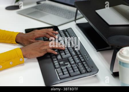 African American man sitting at white desk in home office typing on black wireless keyboard Stock Photo