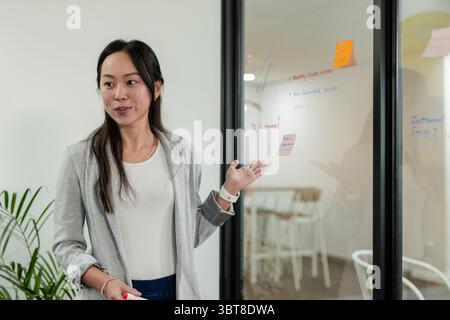 Asian businesswoman holding red marker leading session at office glass wall with sticky notes Stock Photo