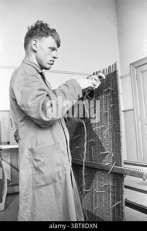 Staff of the Haarlem Work Facility for the disabled at Botermarkt 6 do various activities crafts social work Haarlem Botermarkt The Netherlands, Whizgle News, Dutch Desk, The Netherlands, 1950 - 2000 on 03-08-1964. These topics are shown in the image. In a well-lit room with a neutral color palette, a young man focuses intently as he works on a textile weaving project. He is dressed in a light-colored, buttoned work coat that appears somewhat oversized, suggesting a utilitarian purpose. His dark hair is slightly tousled, highlighting a youthful yet serious demeanor. The young man stands beside Stock Photo