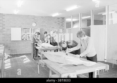 Formation school Velsen Schools, Whizgle News, Dutch Desk, The Netherlands, 1950 - 2000 on 20-03-1969. The image shows these topics. The scene showcases a spacious, well-lit workshop, characterized by a warm, earthy color palette primarily consisting of shades of brown and gray. The walls are made of simple, textured bricks, providing a rustic and industrial backdrop. Large windows allow natural light to pour in, illuminating the space and creating a bright, inviting atmosphere. In the foreground, several sturdy wooden tables are arranged, each occupied by individuals engrossed in various task Stock Photo