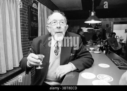 Piet Veldheer HST [Boogovens Chess Tournament], Whizgle News, Dutch Desk, The Netherlands, 1950 - 2000 on 20-01-1992. These topics are shown in the image. In a warmly lit interior, an elderly man sits at the bar, holding a small glass delicately in his hand. He has a thin, white beard and wears a formal, dark blazer over a light-colored sweater, giving him an air of distinguished charm. His round glasses rest on his nose, and he gazes thoughtfully off to the side, suggesting introspection or reminiscing. The bar itself is sleek and modern, with a polished surface reflecting the soft ambient li Stock Photo