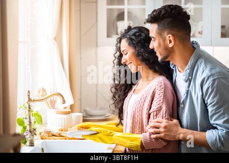 Portrait Of Happy Young Middle-Eastern Spouses Washing Dishes After Lunch In Kitchen Stock Photo