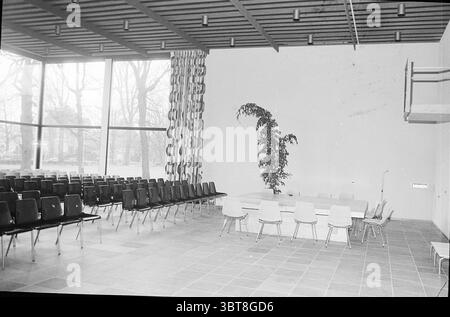 Interior Council Chamber etc. new Heemstede Town Hall. Heemstede Municipal Council, Whizgle News, Dutch Desk, The Netherlands, 1950 - 2000 on 10-12-1973. These are the topics in the image. The scene depicts a spacious interior characterized by a minimalist, modern design. On one side, sleek black chairs with a simple, angular silhouette are arranged in neat rows, creating a sense of order and functionality. Their dark hue stands out against the lighter tones of the room. In the center, a large, rectangular table with a smooth surface serves as a focal point. Around it, a mix of chairs in soft Stock Photo