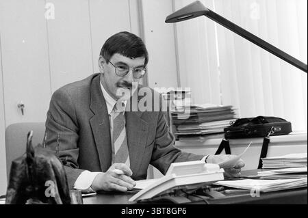 Mr. G. Titulaer general secretary WLTO [Western Agriculture and Horticulture Organization], Whizgle News, Dutch Desk, The Netherlands, 1950 - 2000 on 06-04-1997. These are the topics in the image. The scene depicts a middle-aged man seated at a desk in a well-organized office space. He has a neatly combed hairstyle and wears glasses, which accentuate his approachable demeanor. His attire consists of a light gray suit with subtle pinstripes and a pastel-colored tie that adds a soft contrast to his outfit. The desk is cluttered but not chaotic, featuring an assortment of stacked papers, a deskto Stock Photo