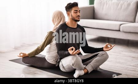 Young Middle Eastern Spouses Meditating Together On Mat In Living Room Stock Photo