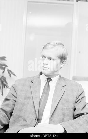 Gerrit Peijs football player DWS Football, Whizgle News, Dutch Desk, The Netherlands, 1950 - 2000 on 06-07-1965. These are the topics in the image. The scene features a young man seated, characterized by his straight, light blonde hair. He wears a tailored suit jacket in a modest gray shade, complemented by a white shirt and a tie, likely dark in color. The fabric of the suit appears classic and formal, indicative of a business or professional setting. His expression is contemplative, with a slight furrow in his brow, suggesting thoughtfulness or introspection. The lighting is soft and diffuse Stock Photo
