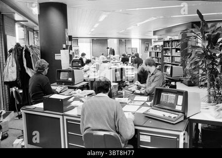 Editorial HD Haarlems Dagblad etc. and IJmuider Courant and Koeri, Whizgle News, Dutch Desk, The Netherlands, 1950 - 2000 on 29-01-1986. The image contains these topics. The scene features a busy office environment filled with multiple workstations. Several individuals are seated at desks, focusing intently on their computer screens. The color palette is predominantly monochromatic, showcasing various shades of gray and black, creating a serious, professional atmosphere. The desks are cluttered with papers, notes, and personal items, indicating active engagement with ongoing projects. In the b Stock Photo