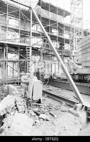 Renovation of buildings Zijlstraat Haarlem Haarlem Zijlstraat The Netherlands, Whizgle News, Dutch Desk, The Netherlands, 1950 - 2000 in 1982. These are the topics in the image. The scene depicts a construction site characterized by a mix of industrial elements and a sense of ongoing labor. The environment is dominated by scaffolding, which forms a framework around the partially constructed building. Metal beams and wooden planks intersect at various angles, creating a complex structure that hints at both stability and chaos. Scattered throughout the ground are piles of debris, including brick Stock Photo