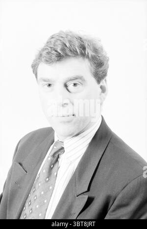 Portraits Chamber of Commerce in Haarlem Haarlem The Netherlands, Whizgle News, Dutch Desk, The Netherlands, 1950 - 2000 on 21-01-1996. The image contains these topics. The scene features a man with a medium-length, wavy hairstyle that appears to be a shade of dark brown. He is dressed in a formal black suit jacket over a white, collared shirt, complemented by a patterned tie that incorporates tones of blue and maroon. His expression is somewhat neutral, conveying a sense of professionalism or introspection. The background is entirely white, creating a striking contrast with his outfit and emp Stock Photo
