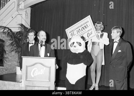 Royal decoration Mrs. Claus H'dorp Hoofddorp The Netherlands, Whizgle News, Dutch Desk, The Netherlands, 1950 - 2000 on 25-09-1994. The image includes these topics. The scene is set in a stylishly decorated venue, exuding a sense of elegance and celebration. Rich, dark curtains drape in the background, creating a striking contrast against the bright lights illuminating the area. In the forefront, a man stands confidently at a wooden podium, dressed in a tuxedo. His expression conveys a mix of excitement and professionalism as he addresses the audience. To his left, a costumed individual dresse Stock Photo