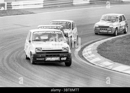 Formula I evening + Fuego Renault, Whizgle News, Dutch Desk, The Netherlands, 1950 - 2000 on 01-09-1980. The image contains these topics. The scene captures a dynamic moment on a racetrack, filled with excitement and motion. Three compact cars are in close proximity, each showcasing distinct designs and colors. The lead car, adorned in a striking white and adorned with racing sponsor stickers, appears to be gaining speed around a sharp curve. Its front end is low to the ground, giving it an aggressive stance. The second car follows closely, featuring a predominantly dark color with bold accent Stock Photo