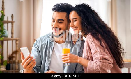 Happy Middle Eastern Couple Browsing Internet On Smartphone While Having Breakfast Stock Photo