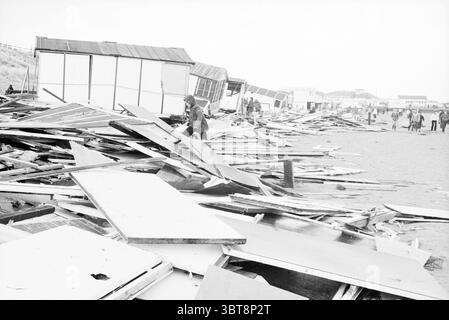 Storm beach IJmuiden Storm and storm damage Beach and beaches IJmuiden The Netherlands, Whizgle News, Dutch Desk, The Netherlands, 1950 - 2000 on 19-04-1980. These topics appear in the image. The scene depicts a devastated beach area, where large, scattered pieces of wood and debris dominate the foreground. The remnants of structures, possibly beach huts or cabins, lie in disarray, their exteriors weathered and worn. Some fragments may appear splintered, emphasizing the impact of recent turmoil. The ground is a blend of sandy tones intermingled with the tumbled debris, creating a stark contras Stock Photo