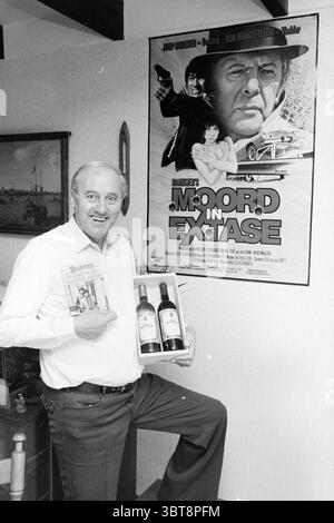 Adjutant Baantjer detective and writer of books Writing People Police, Whizgle News, Dutch Desk, The Netherlands, 1950 - 2000 on 25-01-1984. These topics appear in the image. In a domestic interior, a man stands confidently with a broad smile, his posture suggesting pride and excitement. He is dressed in a light-colored shirt, and his stance is casual, with one arm raised to hold a wooden box containing bottles of wine, while his other hand supports a smaller package. The setting is characterized by a cozy atmosphere, with warm lighting casting soft shadows that enhance the feel of home. Behin Stock Photo