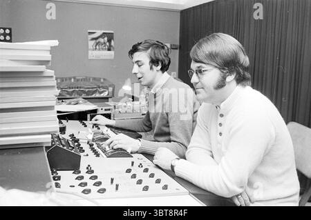 Tim Griek Bovema Music People, Whizgle News, Dutch Desk, The Netherlands, 1950 - 2000 on 07-04-1970. These are the elements in the image. In a cozy recording studio, two men are engaged in the process of music production. The room has a warm, intimate atmosphere, accented by the soft glow of studio lights. The first individual, seated on the left, has dark, wavy hair and is dressed in a medium grey sweater. He is focused, adjusting knobs and faders on the equipment in front of him. His expression suggests concentration and enthusiasm for the task at hand. Next to him is the second individual, Stock Photo