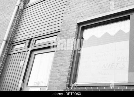 Sign from Marumstraat 'nothing left to get' Signs Haarlem Van Marumstraat The Netherlands, Whizgle News, Dutch Desk, The Netherlands, 1950 - 2000 on 13-02-1986. These are the topics in the image. The scene depicts a building facade characterized by a combination of muted tones and warm textures. A solid brick wall creates a rich and earthy backdrop with varying shades of red and brown. Vertical wooden panels adorn the upper section, contrasting with the brick and providing a modern touch to the structure. To the left, a doorway, framed with a simple but elegantly dark-colored surround, leads i Stock Photo