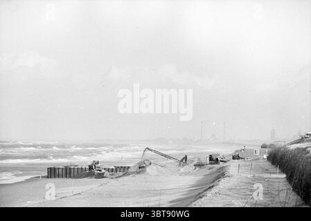 Clearing up explosives on Bloemendaal beach Bloemendaal, Whizgle News, Dutch Desk, The Netherlands, 1950 - 2000 on 11-01-1993. The image contains these topics. The scene presents a coastal view characterized by a muted, monochromatic palette. Soft, gray tones dominate the landscape, evoking a sense of stillness and introspection. The shoreline is marked by rolling waves that crash gently against the sandy beach, their frothy edges blending into the sandy hues. In the foreground, heavy machinery operates, likely involved in dredging or construction, with elongated shadows stretching behind them Stock Photo