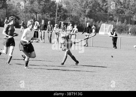 Strawberries - Apeldoorn Hockey, Whizgle News, Dutch Desk, The Netherlands, 1950 - 2000 on 25-09-1983. These topics are shown in the image. The scene captures an energetic moment on a field where a group of players are engaged in a game of field hockey. In the foreground, one player is depicted in mid-swing, fully focused, as they strike the ball with their stick, showcasing determination and athleticism. Their uniform contrasts with the other players; they are dressed in a short, dark skirt and a light-colored top, while another player to the left wears a darker top and matching skirt, creati Stock Photo