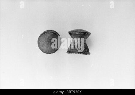 Bullets for the gun, Whizgle News, Dutch Desk, The Netherlands, 1950 - 2000 in 1965. These are the topics in the image. The scene features two distinct objects positioned against a neutral background, creating a minimalist aesthetic. On the left, there is a spherical object, appearing smooth with a matte texture, suggesting a certain weight and solidity. Its dark color gives it a subtle, understated elegance. This round form contrasts with the object to its right. Stock Photo
