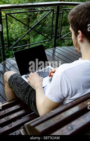 Laptop screen with clear space for client’s photo, as a young man types outdoors in park. Natural light, green background, summer day. Stock Photo