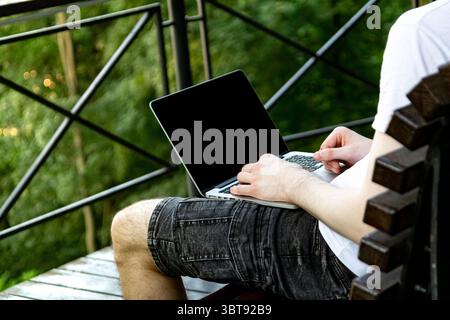 Focus on laptop screen with empty space for photo or content, while a young man in casual outfit works on computer in park. Stock Photo