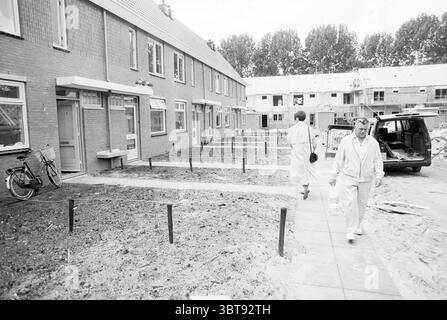 Miscellaneous Romolenpolder New construction, Whizgle News, Dutch Desk, The Netherlands, 1950 - 2000 on 10-07-1989. These topics are shown in the image. The scene presents a residential area characterized by rows of two-story buildings, each with a simple architectural style, primarily constructed from brick. The structures exhibit a muted palette of earthy tones, primarily browns and grays, blending harmoniously with the overcast sky above. In the foreground, two individuals are walking through a well-worn path that cuts through a garden area currently under development, suggesting ongoing co Stock Photo