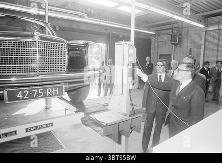 Opening A.N.W.B. techno station. Opening openings commissioning, Whizgle News, Dutch Desk, The Netherlands, 1950 - 2000 on 30-08-1974. These topics appear in the image. The scene features a classic black Mercedes-Benz prominently displayed, elevated on a lift in a well-lit workshop environment. The car's sleek design is accentuated by its shiny surface, reflecting overhead lighting. Surrounding the vehicle are several men in formal attire, including suits and ties, who appear to be engaged in discussion or observing the lift operation closely. The setting has a modern, industrial feel, charact Stock Photo
