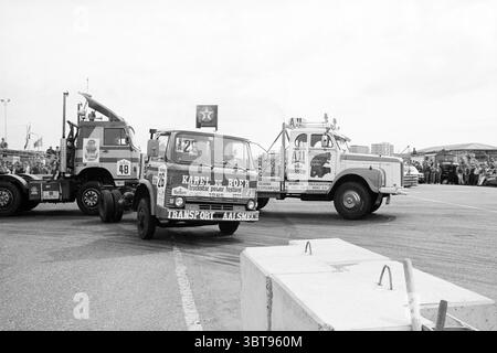 Truck race Zandvoort circuit Circuit Zandvoort Zandvoort, Whizgle News, Dutch Desk, The Netherlands, 1950 - 2000 on 24-06-1985. These are the elements in the image. The scene showcases a vibrant and dynamic competition between two trucks in an outdoor setting, likely at a motorsport event. Both vehicles stand prominently in the foreground, displaying contrasting designs. The truck on the left is adorned with bold graphics and the number '26,' surrounded by an array of colorful logos and branding, lending an energetic feel. Its paint is likely bright and eye-catching, enhanced by the sunlight. Stock Photo