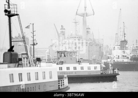 Mighty Servant IJmuiden IJmuiden The Netherlands, Whizgle News, Dutch Desk, The Netherlands, 1950 - 2000 on 28-10-1993. These are the elements in the image. The scene depicts a bustling harbor under a misty atmosphere, where the horizon is shrouded in a soft haze that diffuses light and creates a dreamy ambiance. Two ferries, identifiable by their distinct shapes and markings, occupy the foreground, with their contrasting shades of white and gray standing out against the muted backdrop. The first ferry in view is labeled with a number, providing a focal point, while the other ferry appears sli Stock Photo