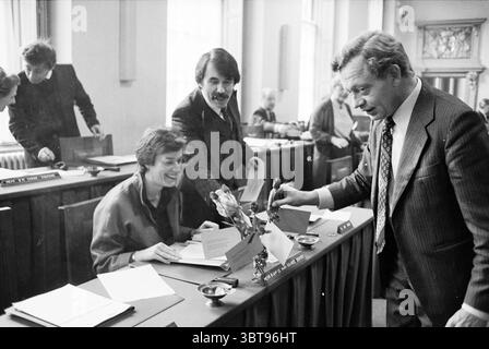 Roses + letter in Haarlem council chamber + councilor Haarlem Municipal Council Haarlem The Netherlands, Whizgle News, Dutch Desk, The Netherlands, 1950 - 2000 on 30-01-1980. These are the topics in the image. The scene captures a lively and engaging atmosphere in a formal setting, likely within a meeting room or legislative assembly. The central focus revolves around a group of individuals engaged in discussion or collaborative work. Several people are seated at long tables, which are draped with muted-colored tablecloths. Some individuals appear to be conversing animatedly, while others are Stock Photo
