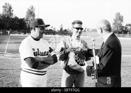 Honoring Hein 3rd base Baseball, Whizgle News, Dutch Desk, The Netherlands, 1950 - 2000 on 17-08-1988. These topics are shown in the image. In a lively outdoor baseball setting, two individuals stand on a neatly maintained field. The backdrop features a well-kept diamond with a bright green outfield, flanked by trees that provide a burst of rich green foliage. One of the men, dressed in a classic white baseball jersey with a dark cap, exudes a confident but friendly demeanor. His uniform shows a subtle sheen, suggesting it's either freshly laundered or well cared for. The other man, wearing su Stock Photo