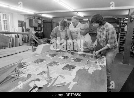Four detectives investigate hashish seizure in a warehouse space Haarlem The Netherlands, Whizgle News, Dutch Desk, The Netherlands, 1950 - 2000 on 07-08-1987. These are the topics in the image. In a spacious workshop filled with wooden materials and tools, four individuals gather around a large, wooden workbench. The dominant color scheme features earthy tones—rich browns from the wood, muted grays, and the occasional splash of white. The walls are lined with shelves brimming with woodworking supplies and equipment, contributing to an industrious atmosphere. The first person, a middle-aged ma Stock Photo