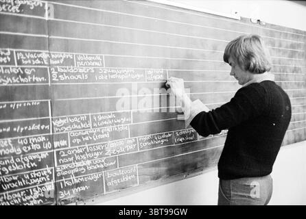 Disaster plan action after North Sea accident Disasters, Whizgle News, Dutch Desk, The Netherlands, 1950 - 2000 on 08-10-1979. These are the topics in the image. In a classroom setting, a woman stands beside a large blackboard filled with chalk writing. She is engaged in writing or erasing something on the board, indicating a teaching or instructional moment. The woman has short, light-colored hair and is dressed in a black sweater, which contrasts with the white walls around her. The blackboard is the focal point of the scene, with various lines of text written in white chalk, displaying diff Stock Photo