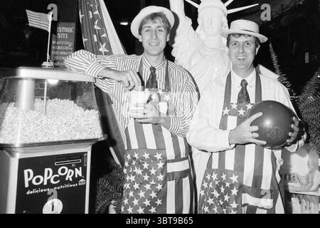 Gebr. Claus due to USA week Claus Party House Bowling Haarlem The Netherlands, Whizgle News, Dutch Desk, The Netherlands, 1950 - 2000 on 20-01-1989. These topics are shown in the image. In a lively indoor setting, two men are positioned in front of a striking figure resembling a well-known statue. The men wear matching outfits composed of white shirts and bold aprons decorated with stars and stripes, reflecting a patriotic theme. Their faces exhibit expressions of cheerfulness as they engage with the viewer, one holding a cup and the other a bowling ball. Adjacent to them, a vintage popcorn ma Stock Photo