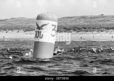 Nautical miles in Bloemendaal aan Zee Bloemendaal, Whizgle News, Dutch Desk, The Netherlands, 1950 - 2000 on 20-08-1994. These topics are shown in the image. The scene is set in a coastal environment, characterized by a gently rippling sea that seems to stretch toward the horizon. In the foreground, several individuals are engaged in an aquatic activity, their heads breaking the surface of the water, each wearing distinct swimming caps, some white and others black. A large buoy, marked with the number '3' and adorned with a simple bird motif, stands prominently in the water. Its cylindrical fo Stock Photo