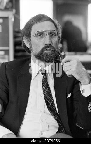 Mr Den Haring Heemsteedse Courant People newspapers and magazines, Whizgle News, Dutch Desk, The Netherlands, 1950 - 2000 on 09-03-1983. These topics are shown in the image. The scene captures a middle-aged man sitting comfortably in a casual yet professional setting. He has a neatly groomed beard and wears a classic black suit jacket over a white dress shirt. A tie featuring a plaid pattern adds a touch of personality, contrasting with the solid colors of his suit. His spectacles rest lightly on his nose, framing his thoughtful expression as he holds a pen close to his mouth, suggesting conte Stock Photo