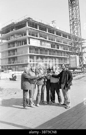 Highest point sister house Highest point, Whizgle News, Dutch Desk, The Netherlands, 1950 - 2000 on 26-05-1972. The image shows these topics. In the foreground, a group of six men stands arm-in-arm, celebrating a significant moment. They have a relaxed demeanor, with smiles on their faces that convey camaraderie. The men wear a mix of casual and semi-formal clothing, consisting of jackets and shirts. Their varying hairstyles and facial hair add individuality to each person. Behind them, a large construction site dominates the scene, showcasing a partially built structure. The building is compo Stock Photo