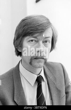 Mr. Verheul General Employers Association Persons Associations, Whizgle News, Dutch Desk, The Netherlands, 1950 - 2000 on 31-01-1985. These topics appear in the image. The scene features a man with a light complexion and a prominent mustache, complemented by a head of medium-length, wavy hair. His expression conveys a sense of seriousness, with a slightly furrowed brow. He is seated, suggesting a moment of contemplation or discussion. He is attired in a classic suit jacket that appears to be a muted shade, possibly gray, and is paired with a light-colored shirt and a tie featuring a simple, da Stock Photo