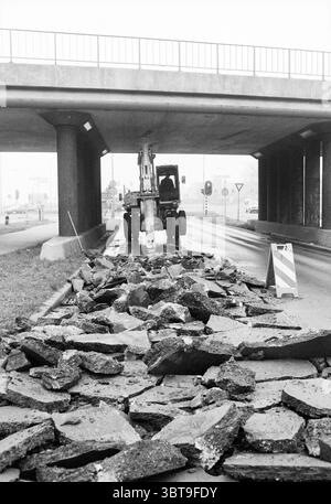 Work at viaduct Noostraat IJmuiden Work IJmuiden De Noostraat The Netherlands, Whizgle News, Dutch Desk, The Netherlands, 1950 - 2000 on 24-01-1989. These are the topics in the image. Beneath a stark concrete overpass, a scene of construction and disruption unfolds. The ground is strewn with large, uneven slabs of broken asphalt, creating a chaotic tapestry of gray shades and jagged edges. The fragments vary in size, some resembling puzzle pieces, accented by the occasional sheen of moisture, suggesting recent rain. In the background, a large, mechanical excavator stands poised, its arm extend Stock Photo