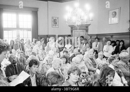 Crowds during hearing Zandvoort town hall Hearing Zandvoort, Whizgle News, Dutch Desk, The Netherlands, 1950 - 2000 on 06-06-1989. The image includes these topics. The scene is set in a large, well-lit room that features high ceilings and wood paneling, giving it an air of formality. Natural light streams in through large windows, casting a soft glow over the gathered individuals. The atmosphere feels tense yet curious, as many faces display a mix of anticipation and concern. A diverse crowd fills the space, with men and women of various ages, each presenting their own unique expressions. Some Stock Photo