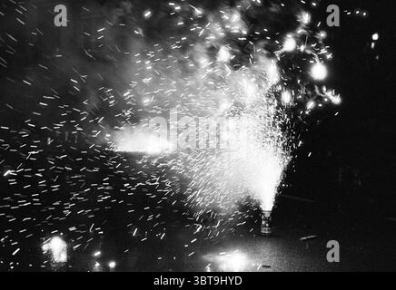 New Year's celebration IJmuiden IJmuiden The Netherlands, Whizgle News, Dutch Desk, The Netherlands, 1950 - 2000 on 30-12-1991. These are the topics in the image. The scene is dominated by a dynamic explosion of light and movement. In the foreground, a fountain of sparks bursts forth from a cylindrical device, sending a cascade of fiery particles into the air. The colors are vibrant, with bright whites and yellows illuminating the dark surroundings, contrasted by deep shadows that envelop the space. The background features a blurred, dimly lit area where more pyrotechnic displays may be taking Stock Photo