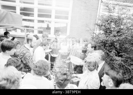 Hungarian children at barbecue Engelmundus Church Lisse Foreigners Food and eateries Lisse, Whizgle News, Dutch Desk, The Netherlands, 1950 - 2000 on 17-04-1989. The image contains these topics. The scene depicts a lively outdoor gathering, likely a barbecue or picnic. Numerous people are gathered around a large grill, enveloped in an atmosphere of camaraderie and enjoyment. In the foreground, there's a diverse group of individuals, ranging in age from children to adults, all engaged in conversation and activity. Many hold plates filled with food, suggesting a communal feast. The faces express Stock Photo