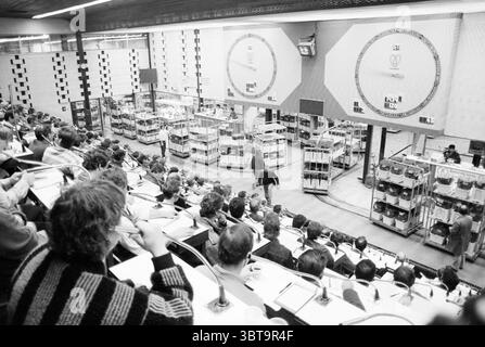 Flower Auction Aalsmeer Auction Aalsmeer, Whizgle News, Dutch Desk, The Netherlands, 1950 - 2000 on 30-10-1987. The image shows these topics. The scene captures a bustling trading floor filled with individuals engaged in intense discussion and observation. Rows of people are seated in a tiered configuration, focusing on the activities in the center of the room. Many are dressed in professional attire, suggesting a formal atmosphere conducive to business dealings. The setting has a modern feel, accentuated by clean lines and a somewhat industrial aesthetic, with metal and glass elements promine Stock Photo
