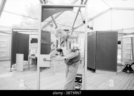 Exhibition custodial sentence Haarlem Police Haarlem The Netherlands, Whizgle News, Dutch Desk, The Netherlands, 1950 - 2000 on 17-07-1994. The image shows these topics. In a spacious, translucent structure, a middle-aged man is engaged in a focused activity. He stands near an industrial-looking door frame, which appears to be part of a larger exhibition or installation. The man, wearing glasses and a collared shirt with contrasting colors—grey and blue—appears to be manipulating a door handle, showcasing a sense of interaction with his surroundings. The setting is minimalist, with several par Stock Photo